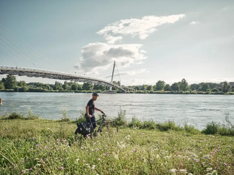 Jobradler schiebt sein Rad in einer Blumenwiese am Flussufer