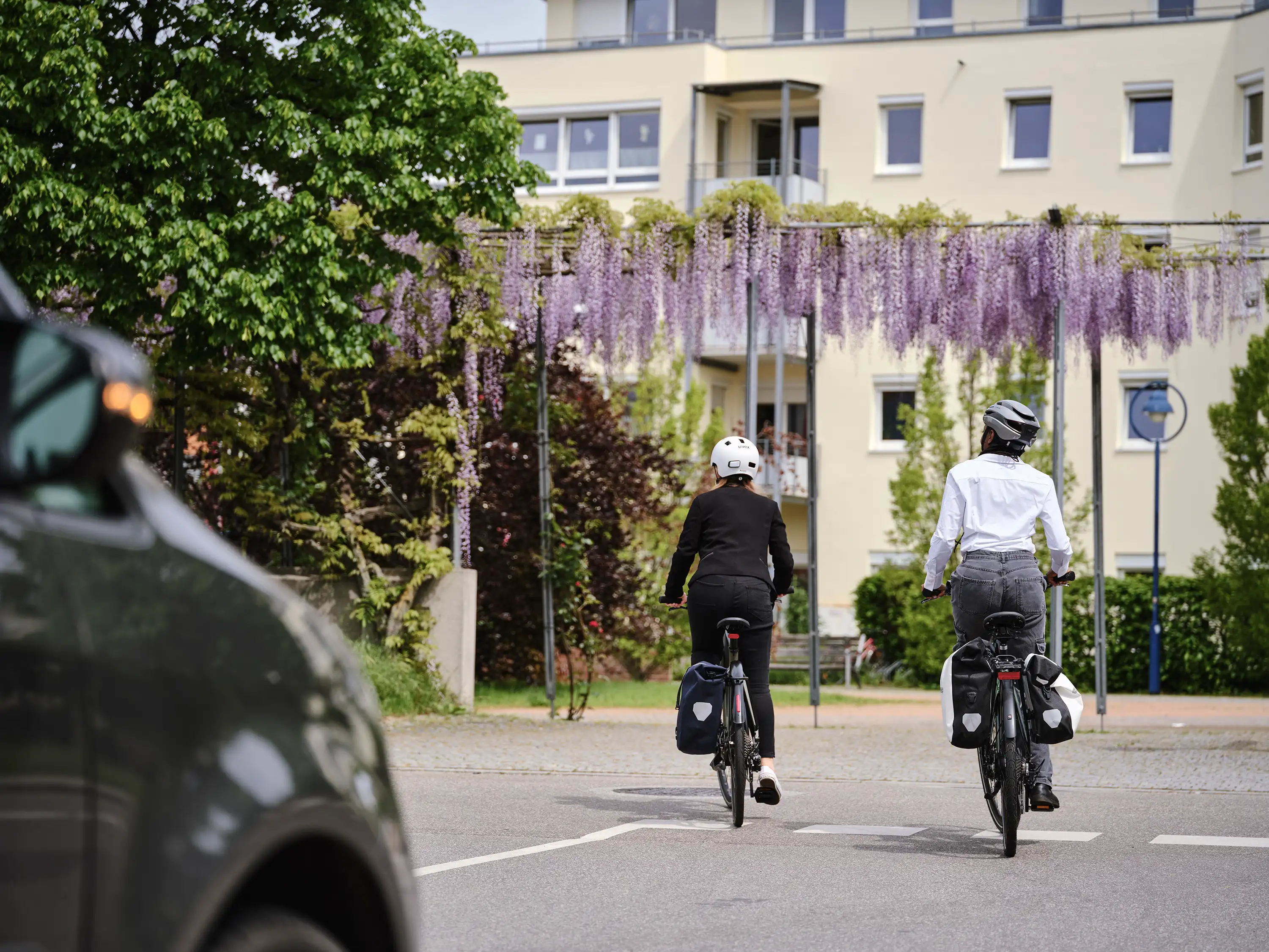 Zwei Jobradlerinnen fahren vom Betrachter weg auf ein Mietshaus zu.